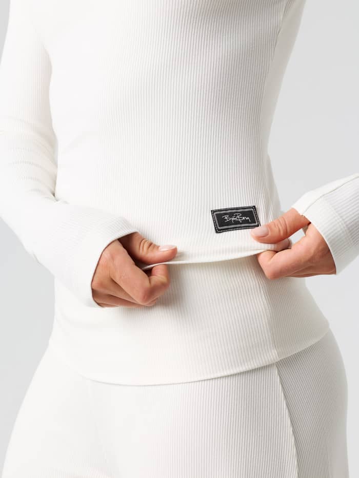 Close-up of the Studio Rib Long Sleeve in Tofu (White) highlighting the ribbed fabric texture and hem logo label.