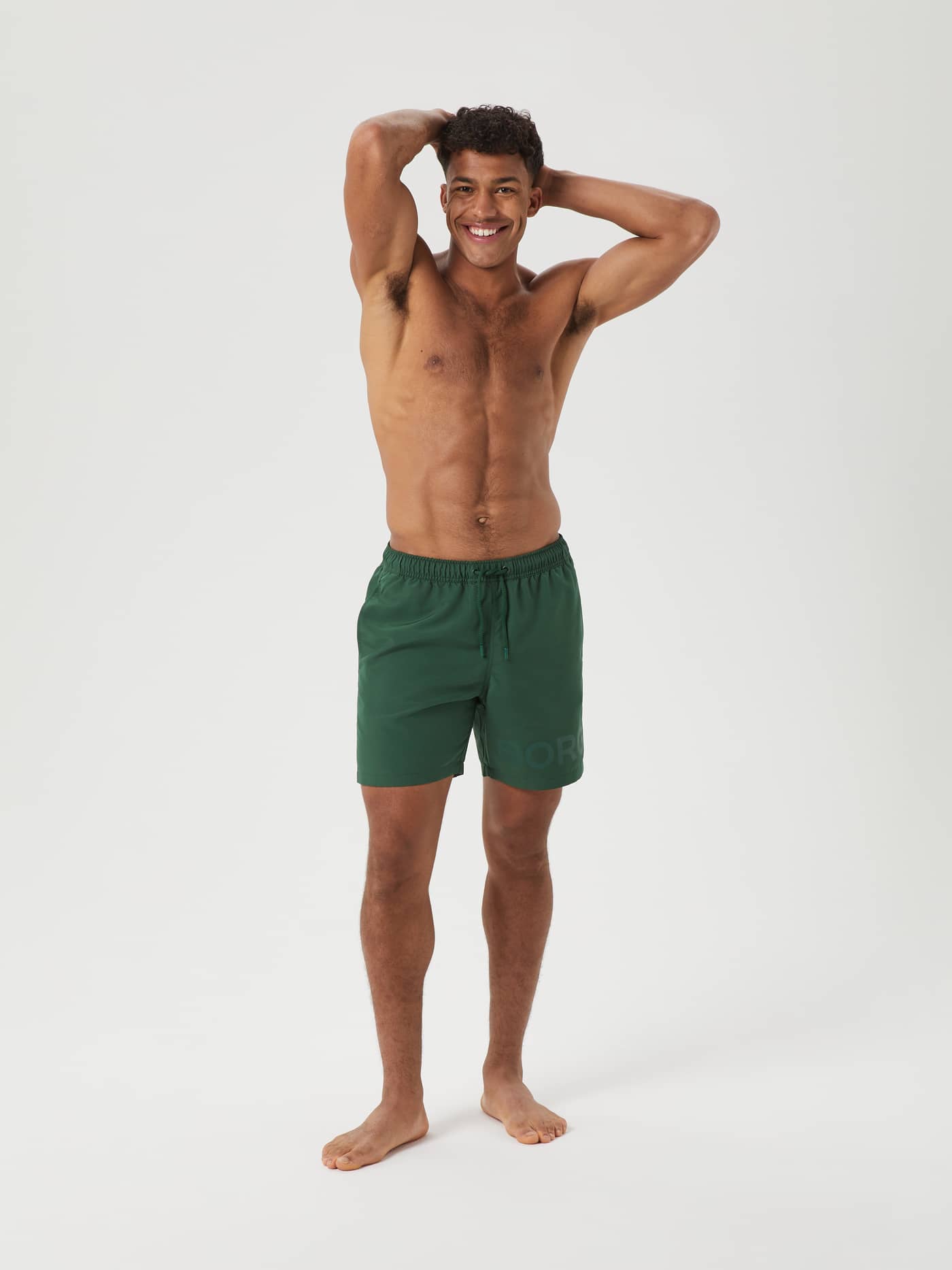 Full-body front view of a man wearing the Björn Borg Swim Shorts in Dark Green (Green) featuring a large tonal logo. - Image 1