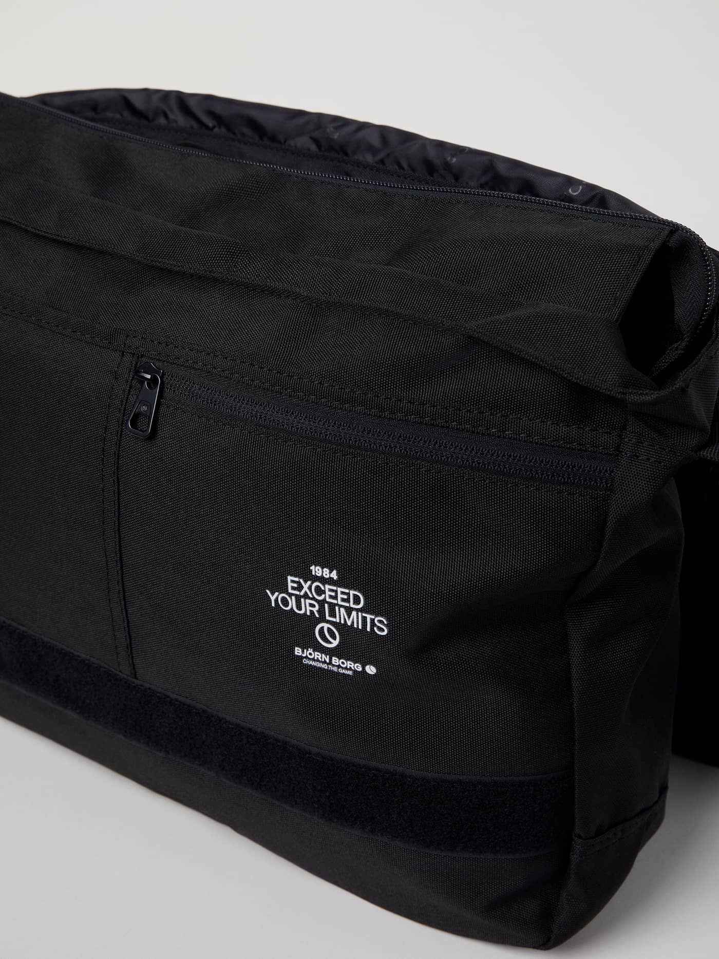 Core Flapbag 12L in zwart gerecycled polyester, close-up van het witte Björn Borg-logo en de rits aan de voorzijde. - Image 9