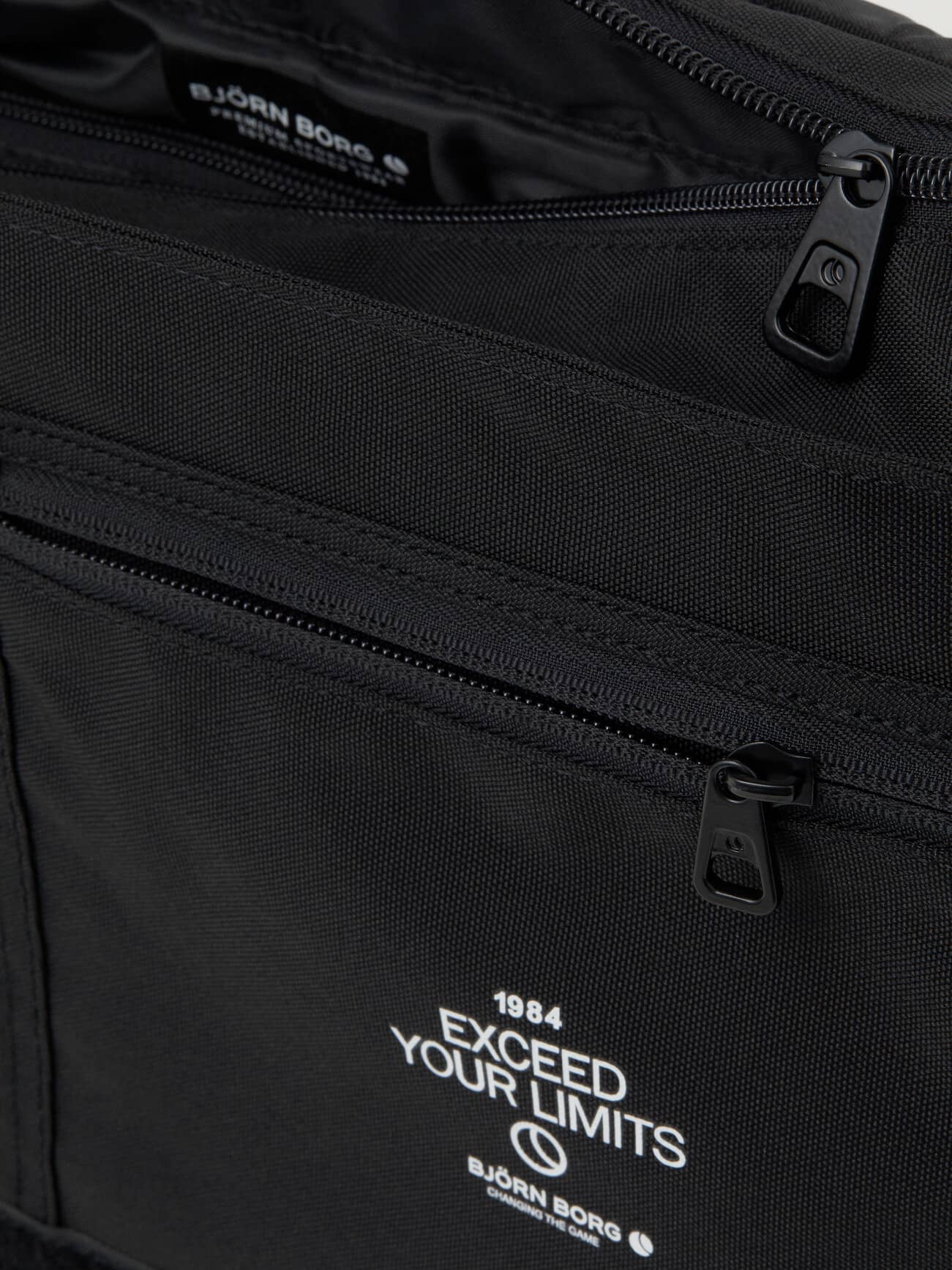 Core Flapbag 12L in Black van polyester met een rits en witte logoprint in detailopname. - Image 5