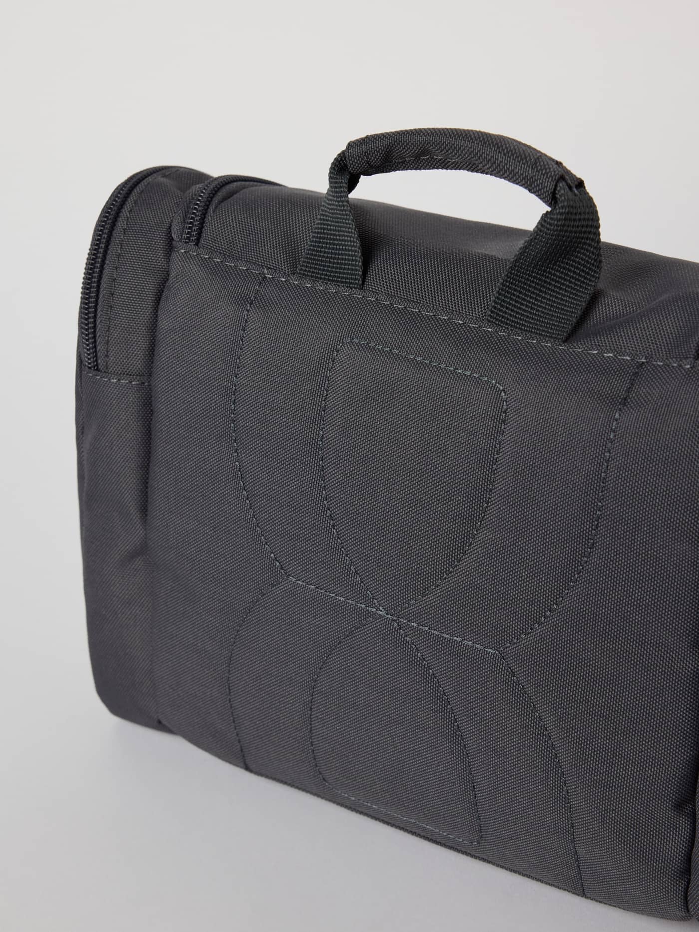 Core Wash Bag Hanging in Asphalt (Grey) featuring a stitched logo and top handle made from durable polyester. - Image 5