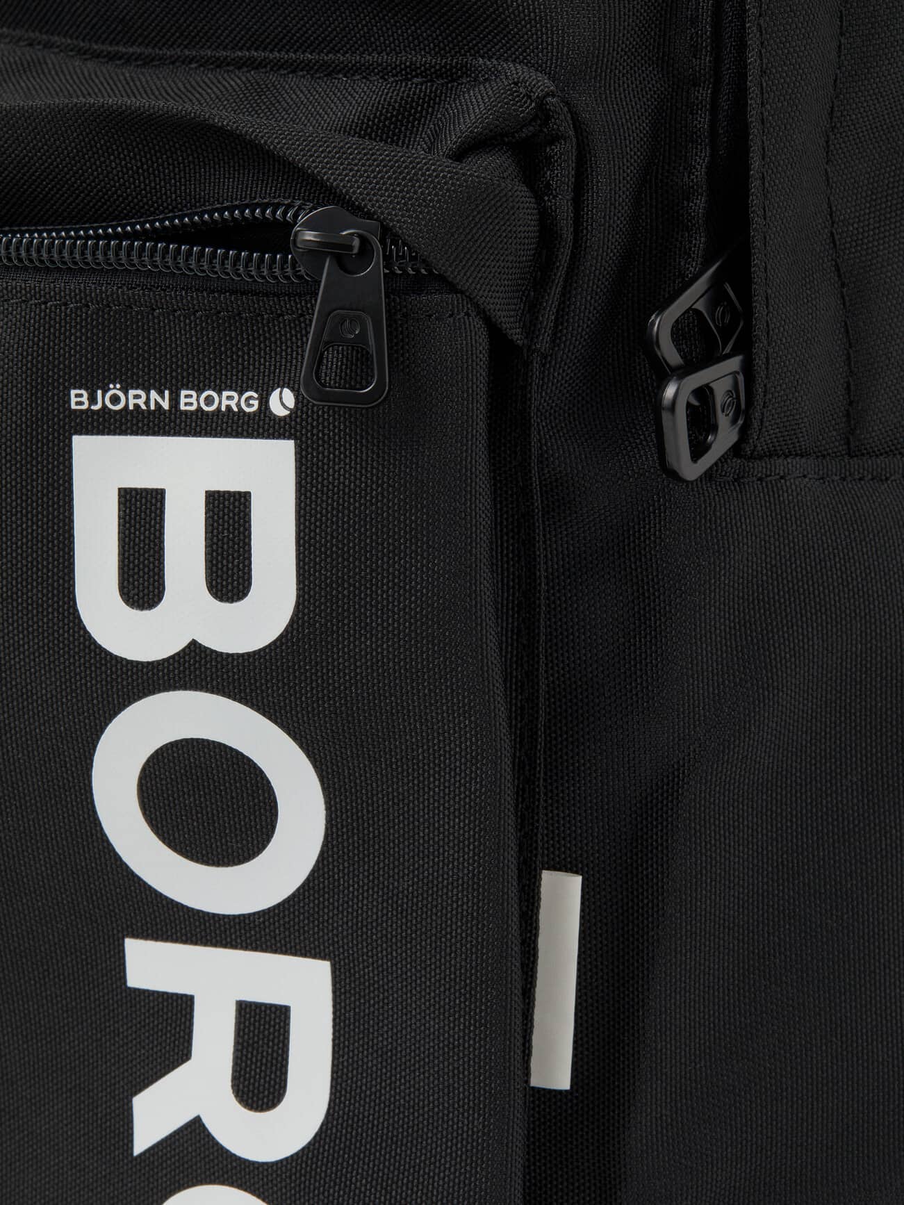 Detailed close-up of the recycled Core Street Backpack 21L in Black, featuring the iconic white Borg logo and zippers. - Image 6
