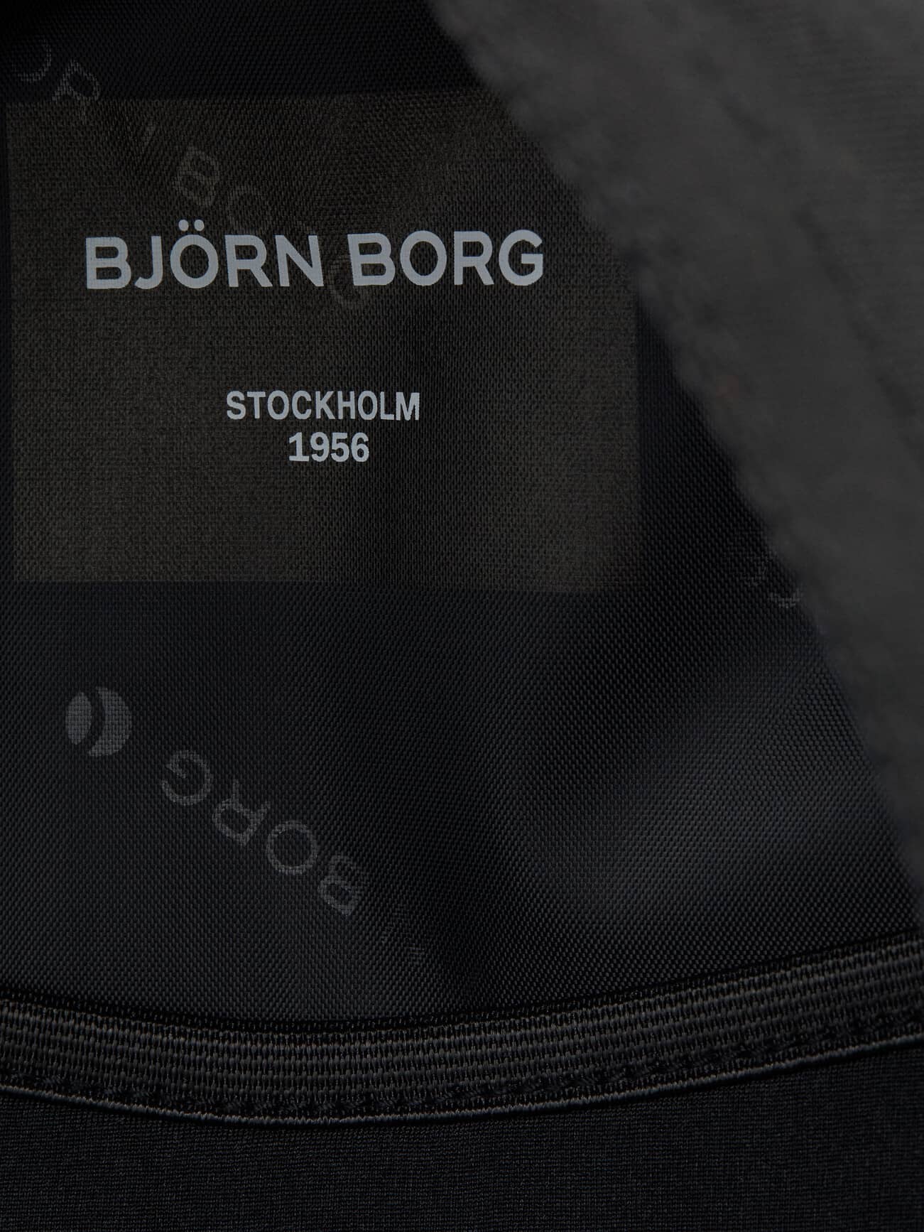 Detailed close-up of the Core Street Backpack 21L in black, showcasing the logo lining and interior brand label. - Image 7