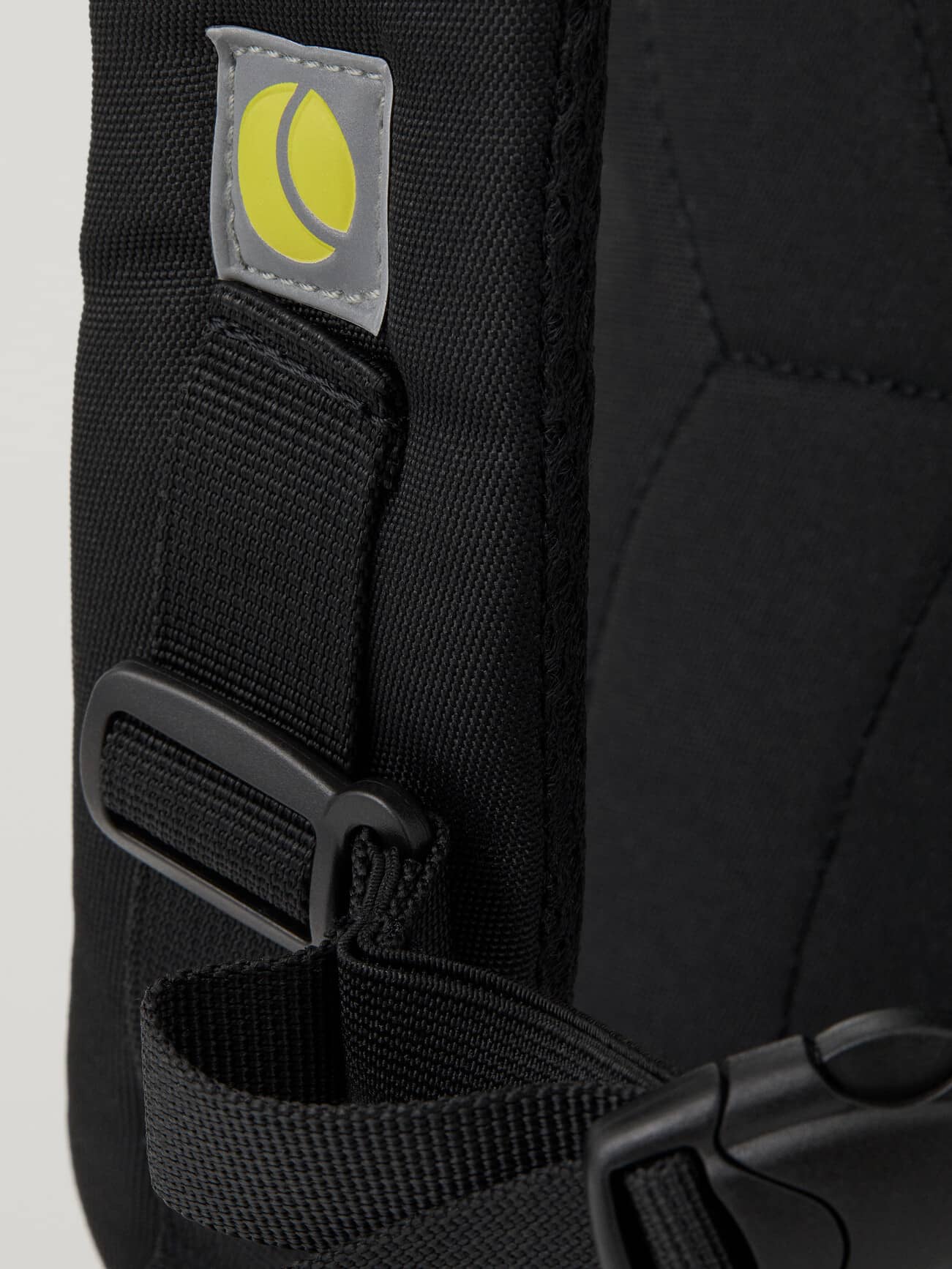 Detailed close-up of the black Core Street Backpack 21L padded strap featuring a reflective yellow tennis ball logo. - Image 8